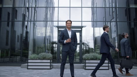 serious manager holding coffee standing at glass office building on lunch break.