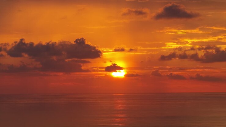 Golden Orange Sunset Over Calm Ocean Water with Clouds