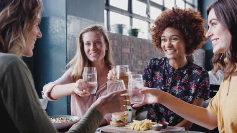 Vier-Junge-Freundinnen-Treffen-Sich-Zu-Getränken-Und-Essen-Und-Stoßen-Im-Restaurant-An