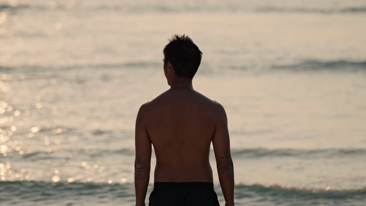 A solitary man stands on a pristine beach in the Maldives, gazing at the vibrant sunset over the calm ocean.