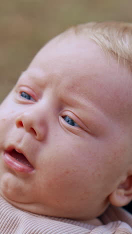 cute serious infant with blonde hair. kid lies on mom's knees and her hands hold baby's cheeks. close up. vertical video