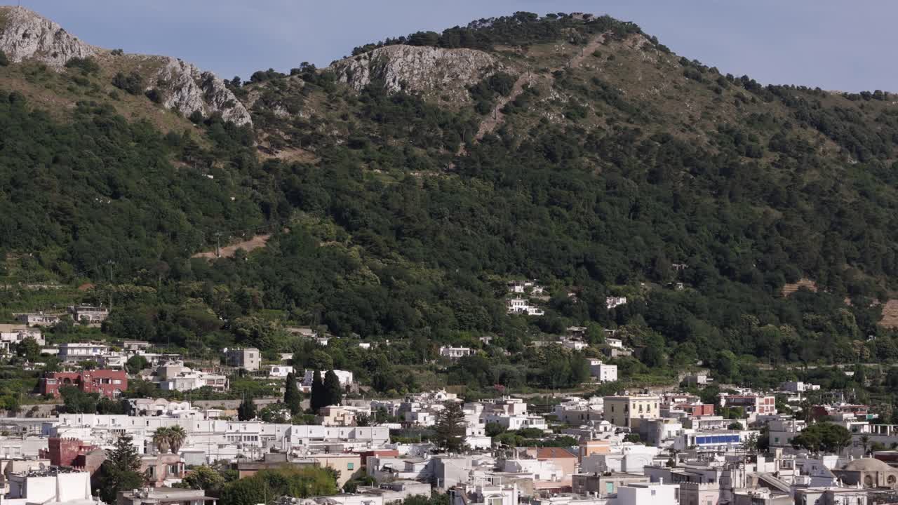 Aerial drone shot panning right, showcasing Anacapri's white houses and mountains in the background on Capri Island
