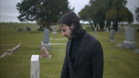 sad, emotional man wearing black suit grieving in graveyard