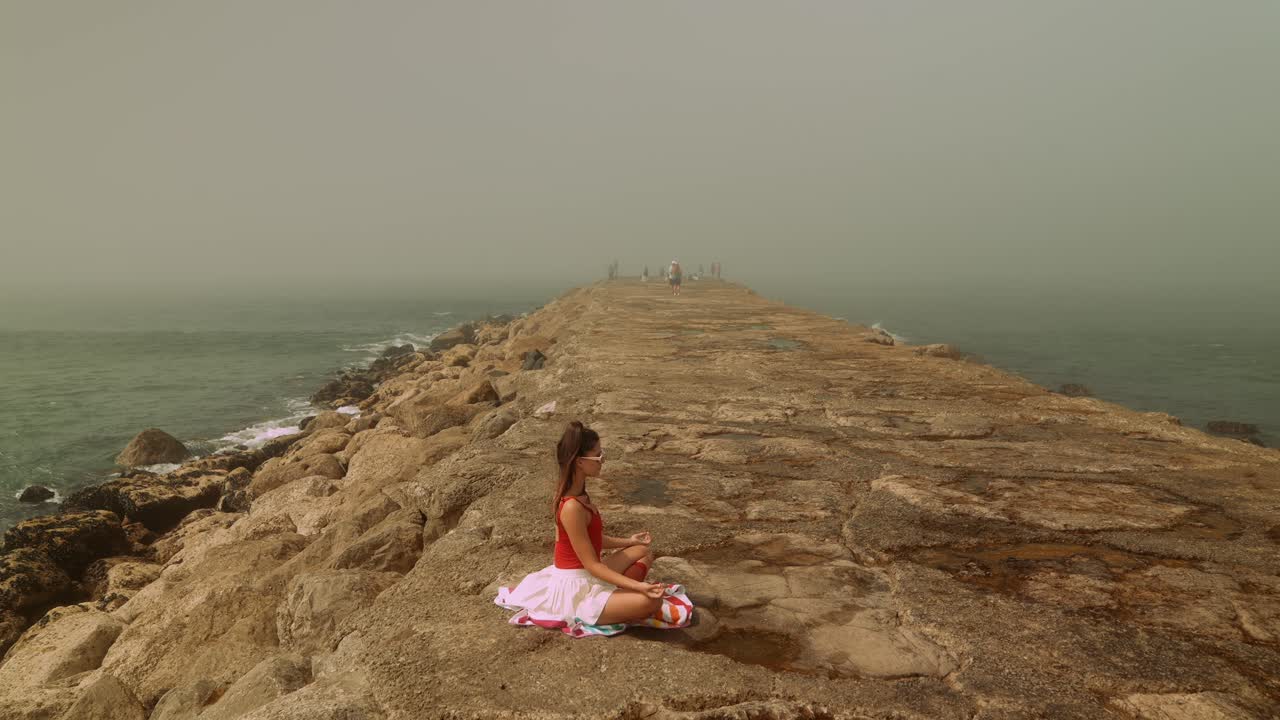 Giovane donna che medita su un molo roccioso in riva all'oceano nella nebbia