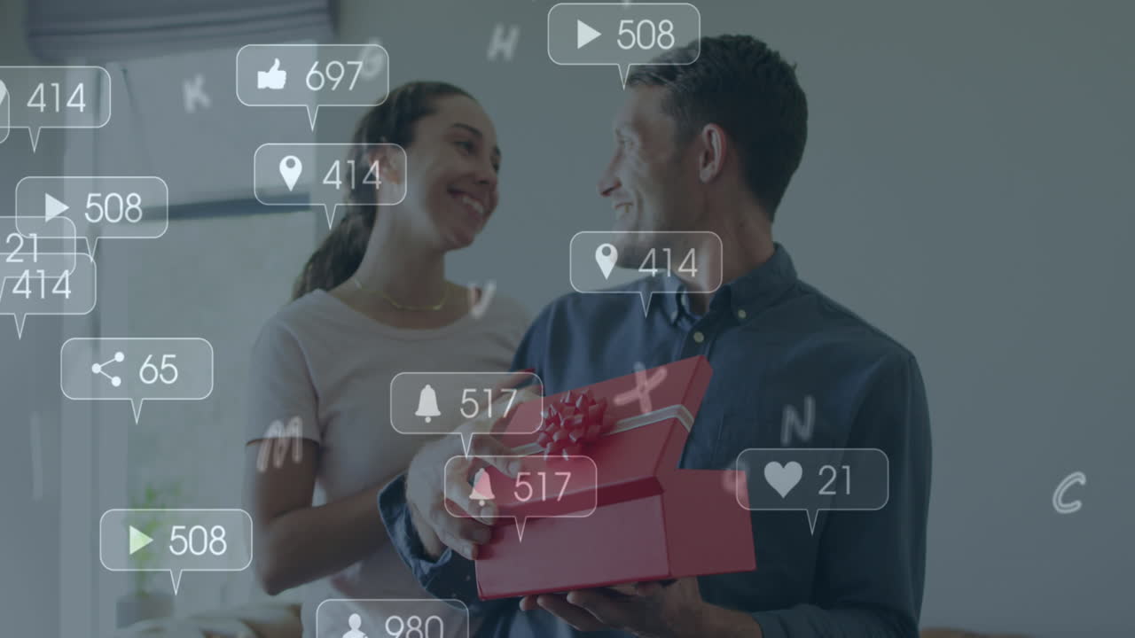 Animation of social media icons over caucasian man opening a box gifted by his home at home