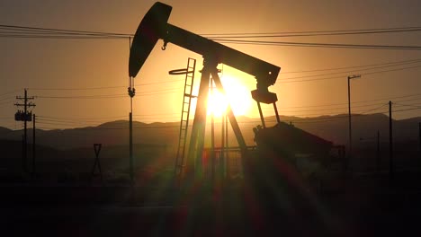 an oil derrick pumps against a sunset sky