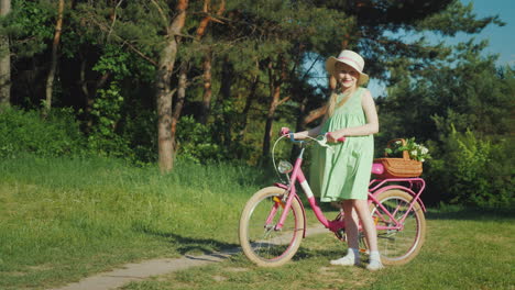 a girl in a summer dress is standing near a bicycle looking at the camera with her basket of wildflo