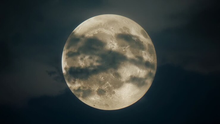 Nuvens passageiras atravessando a superfície da lua cheia no céu noturno, projetando sombras de crateras em movimento