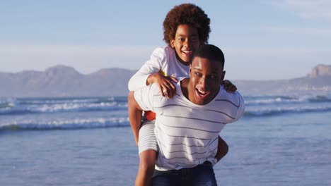 Afroamerikanischer-Vater,-Der-Seinem-Sohn-Am-Strand-Eine-Huckepackfahrt-Gibt