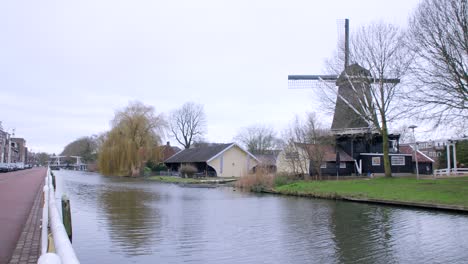 clip de gran angular a lo largo del canal de utrecht en un día nublado brillante, que muestra agua que fluye pacíficamente y un molino de viento tradicional, y un puente en el fondo