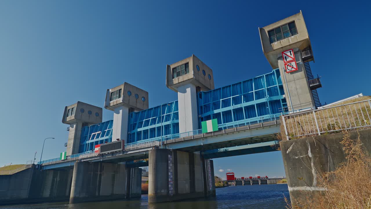 Un'inquadratura grandangolare che mostra la moderna Chiusa di Iwabuchi Blu in primo piano e la storica Vecchia Chiusa Rossa in lontananza. Questo iconico punto di riferimento di Tokyo gestisce l'acqua tra l'Arakawa.