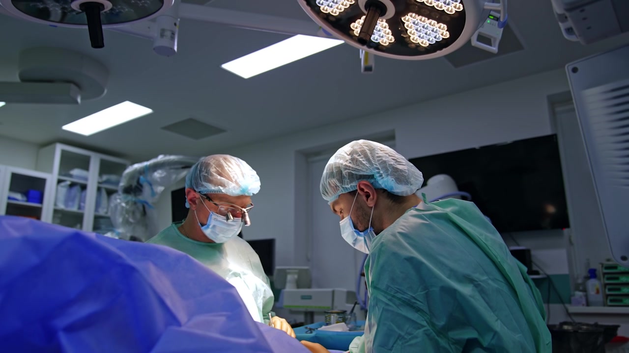 Kaukasiske kirurger opererer patienten under den runde lampe. Overlægen bærer kirurgiske lupper under operationen.