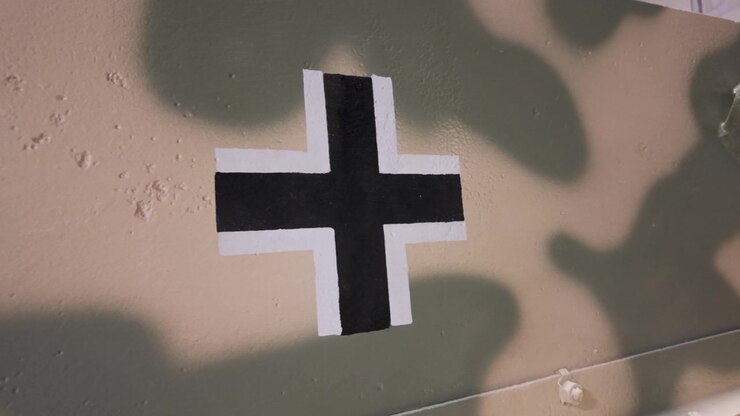 Nærbillede af et sort-hvidt tysk Balkenkreuz-kors, håndmalet på det camouflerede stålpanser på et militærkøretøj fra 2. verdenskrig