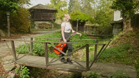 young woman guitarist crosses wooden footbridge bulgarian village