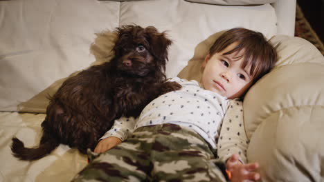 the baby relaxes on the couch, his puppy lies next to him.