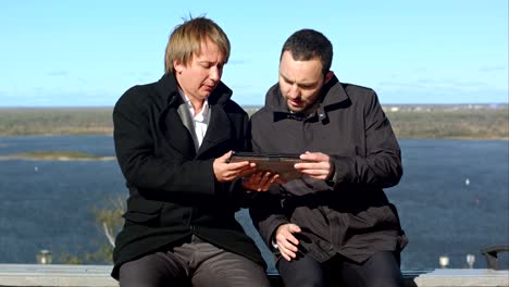 having fun. two man with tablet sitting on bench