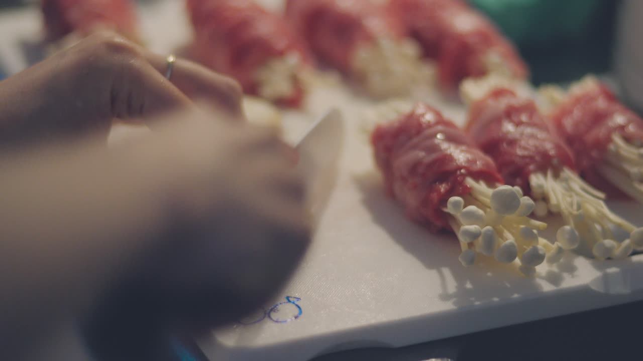 주방장이 쇠고기로 감싼 에노키 버섯을 곁들인 흰색 도마 위에 마늘 클럽을 자르고 있다