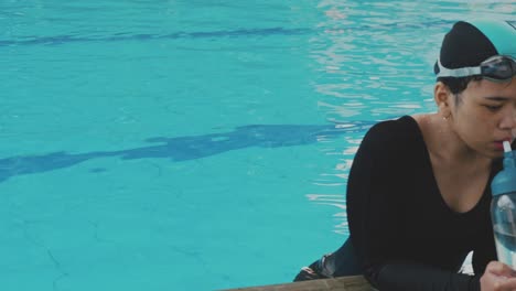 young asian woman swimmer drinking water at pool, hydration and break from workout or training