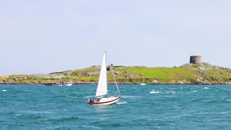 dalkey island is opposite coliemore harbour in dalkey. on a sunny day, a sailboat tries to push through the waves