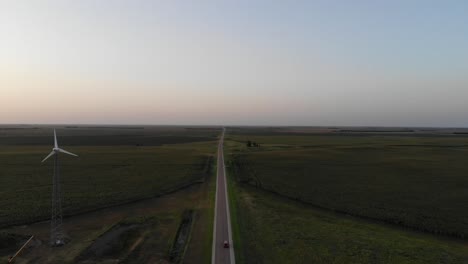 Epic-drone-shot-of-a-highway-with-feilds-a-single-car-and-a-windmill