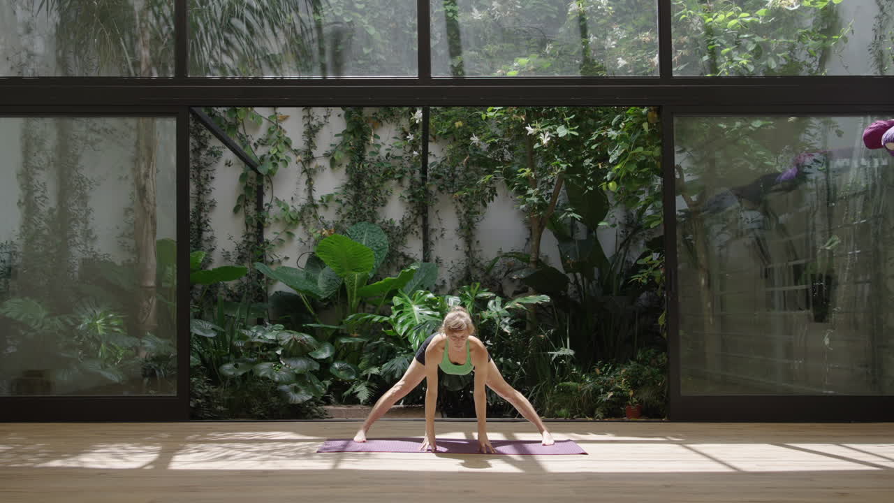 Mulher praticando poses de yoga em um estúdio sereno com vista para o jardim