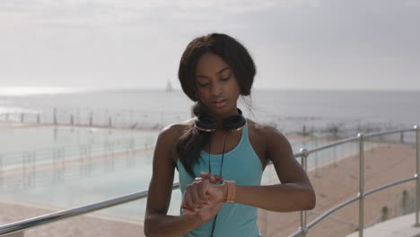 Retrato-De-Una-Joven-Afroamericana-Atlética-Sonriendo-Usando-Un-Reloj-Inteligente-Junto-A-La-Piscina