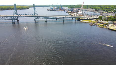 Statische-Drohnenaufnahmen-Der-Sagadahoc-Brücke,-Zwei-Motorboote-Fahren-Entlang-Des-Flusses,-Eines-Fährt-Unter-Der-Brücke-Hindurch