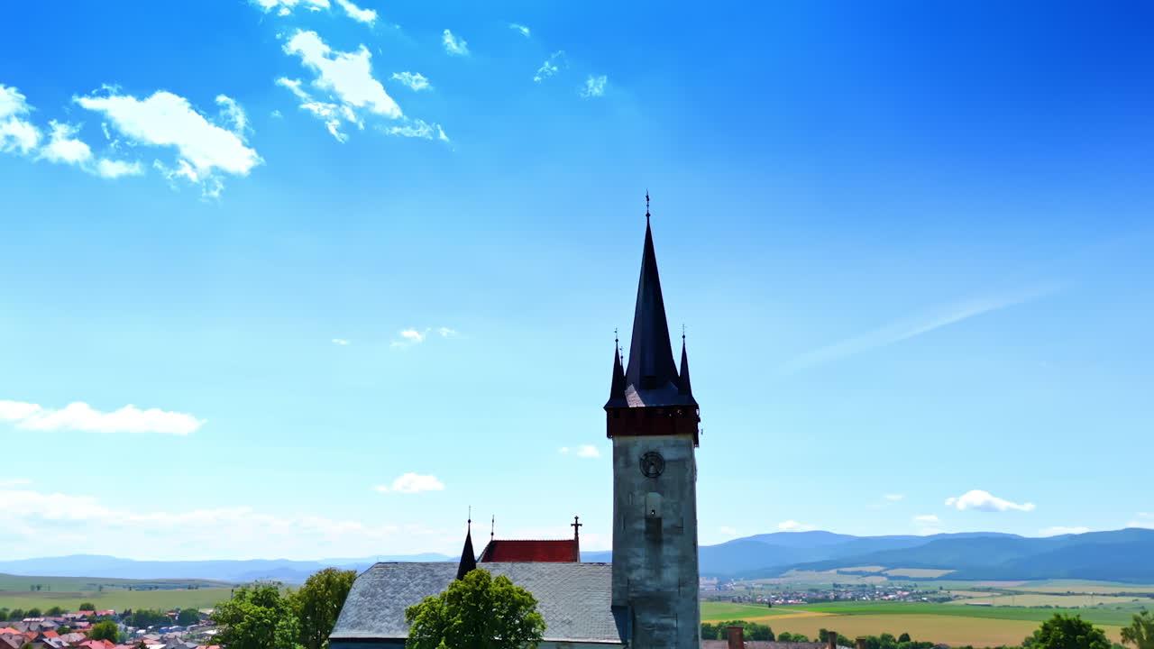 Tower with a clock in the old church with sharp steeples. Drone footage over Slovakia countryside on sunny day