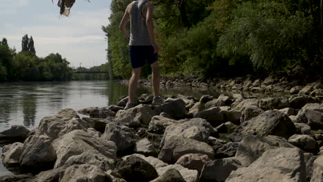 Man-stepping-across-wet-rocks-next-to-a-river-on-a-nature-hike