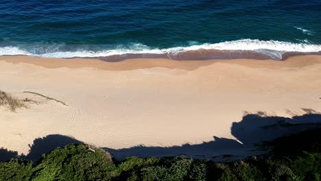 View-from-above-of-a-tilting-drone-overlooking-the-seashore-and-brushes-bushes-tilting-up-towards-the-horizon-with-clear-watery-seas-in-Durban-south-Africa