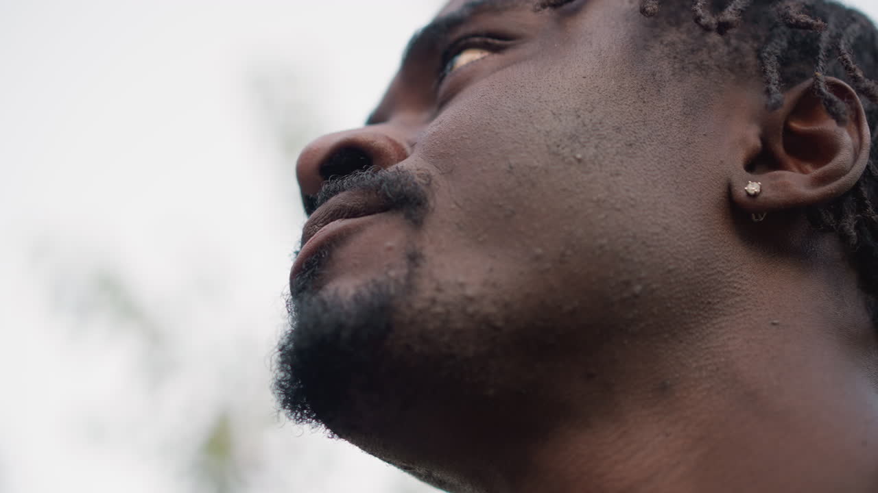 Man drinking beverage, Contemplative man with braided hair sipping pink beverage amongst trees, Outdoor scene featuring thoughtful man with braided hair enjoying pink drink in soft natural light