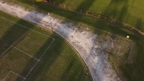 Aerial-tracking-shot-of-slow-person-running-on-sandy-track-around-soccer-field-during-sunset