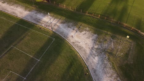 aerial tracking shot of slow person running on sandy track around soccer field during sunset