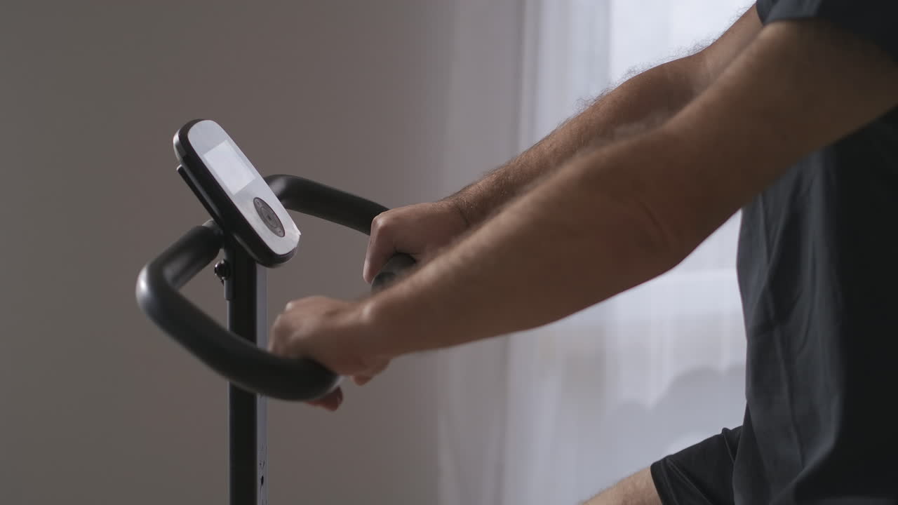 집에서 훈련하는 동안 정지 자전거에 있는 성인 남자의 손 세부 사항 촬영 및 초상화 이동 촬영 건강한 생활 방식과 피트니스