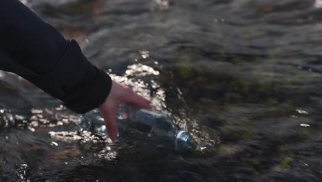 primer plano de una mano femenina llenando una botella de plástico con agua fresca de glaciar proveniente de la cascada bruarfoss en islandia