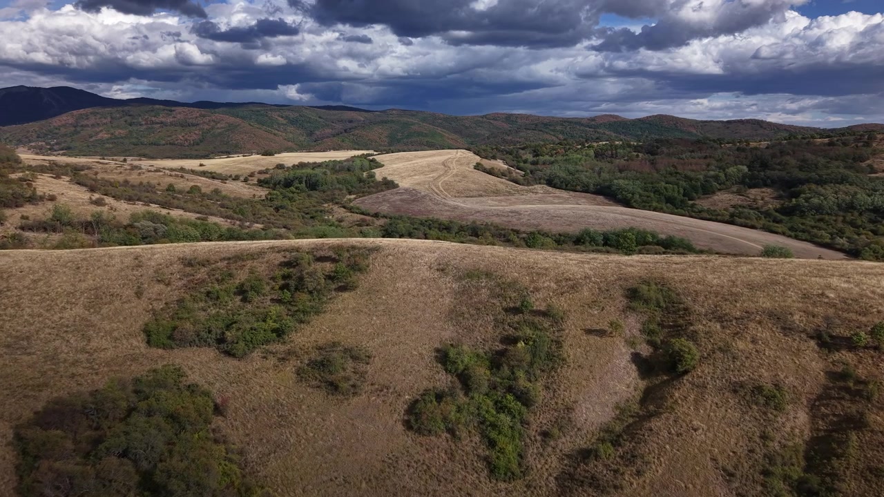 Prospettiva aerea di ampie colline dorate che digradano in una valle profonda sotto un cielo drammatico pieno di nuvole