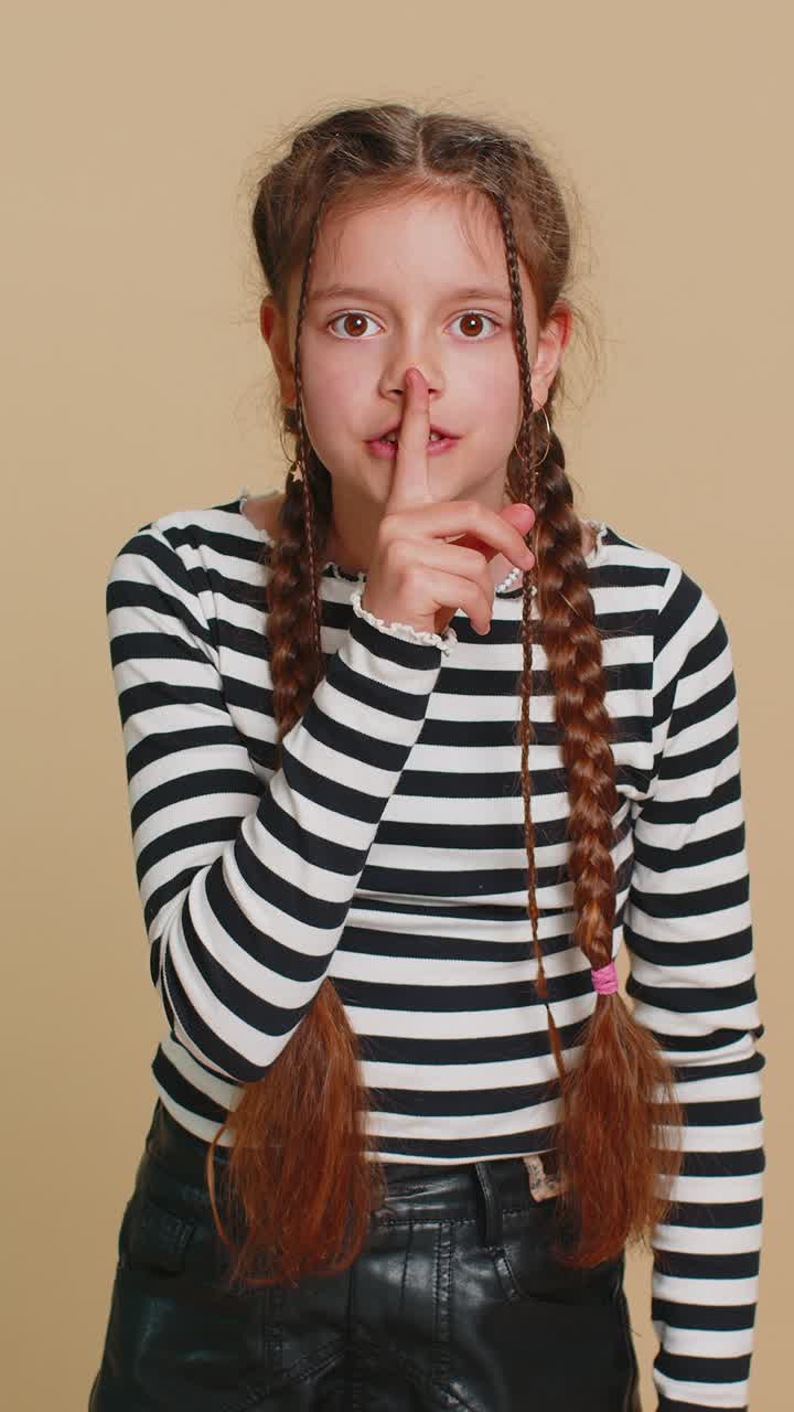 Preteen child girl presses finger to lips makes silence hush sign do not tells gossip secret quiet