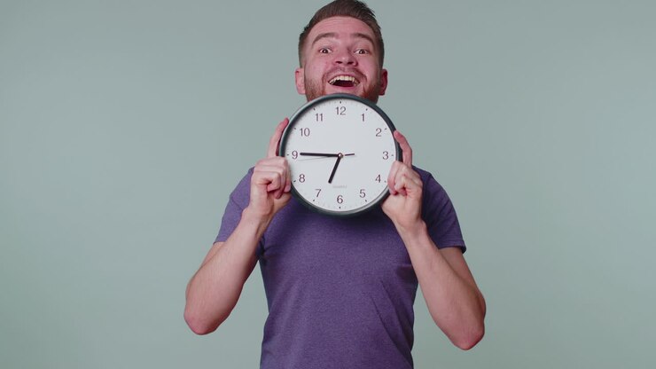 Young man holding clock watch, hiding, checking time on clock, running late to work being in delay