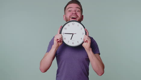 young man holding clock watch, hiding, checking time on clock, running late to work being in delay