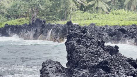 Cinematic-close-up-panning-shot-of-strong-waves-battering-the-lava-rock-along-the-rugged-coast-of-the-Road-to-Hana-in-Maui,-Hawai'i