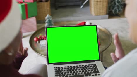 Senior-diverse-couple-in-santa-hats-making-laptop-christmas-video-call,-with-green-screen