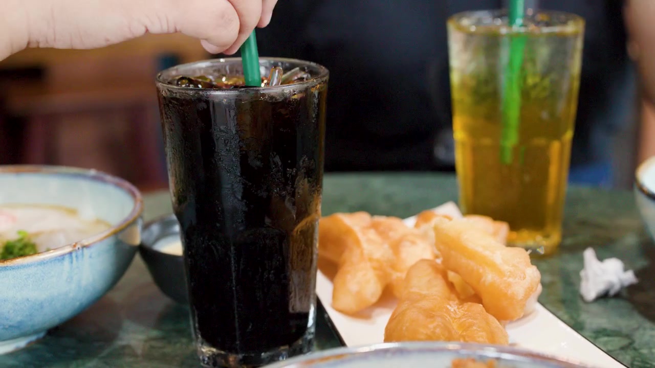 Primo piano della mano di un bambino che mescola e solleva caffè freddo accanto a bastoncini di pasta fritta tradizionali