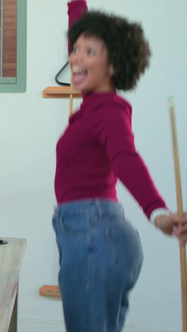 Vertical video: Celebrating maroon-clad woman waving cue, laughing at pool table after sinking ball