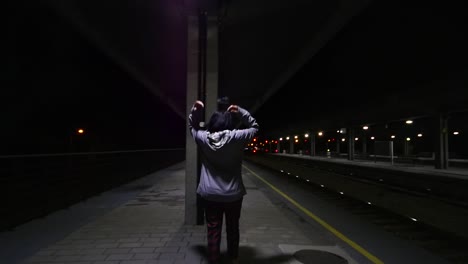 total shot of a girl putting a hoody on a train station at night