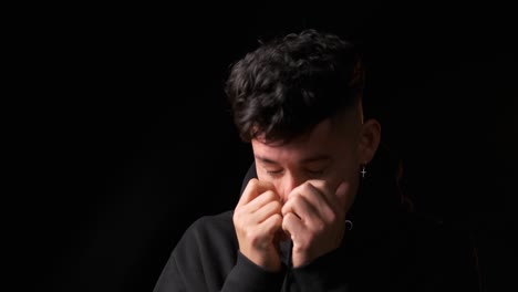 worried man holding and covering his face with his hands while standing over a dark background.
