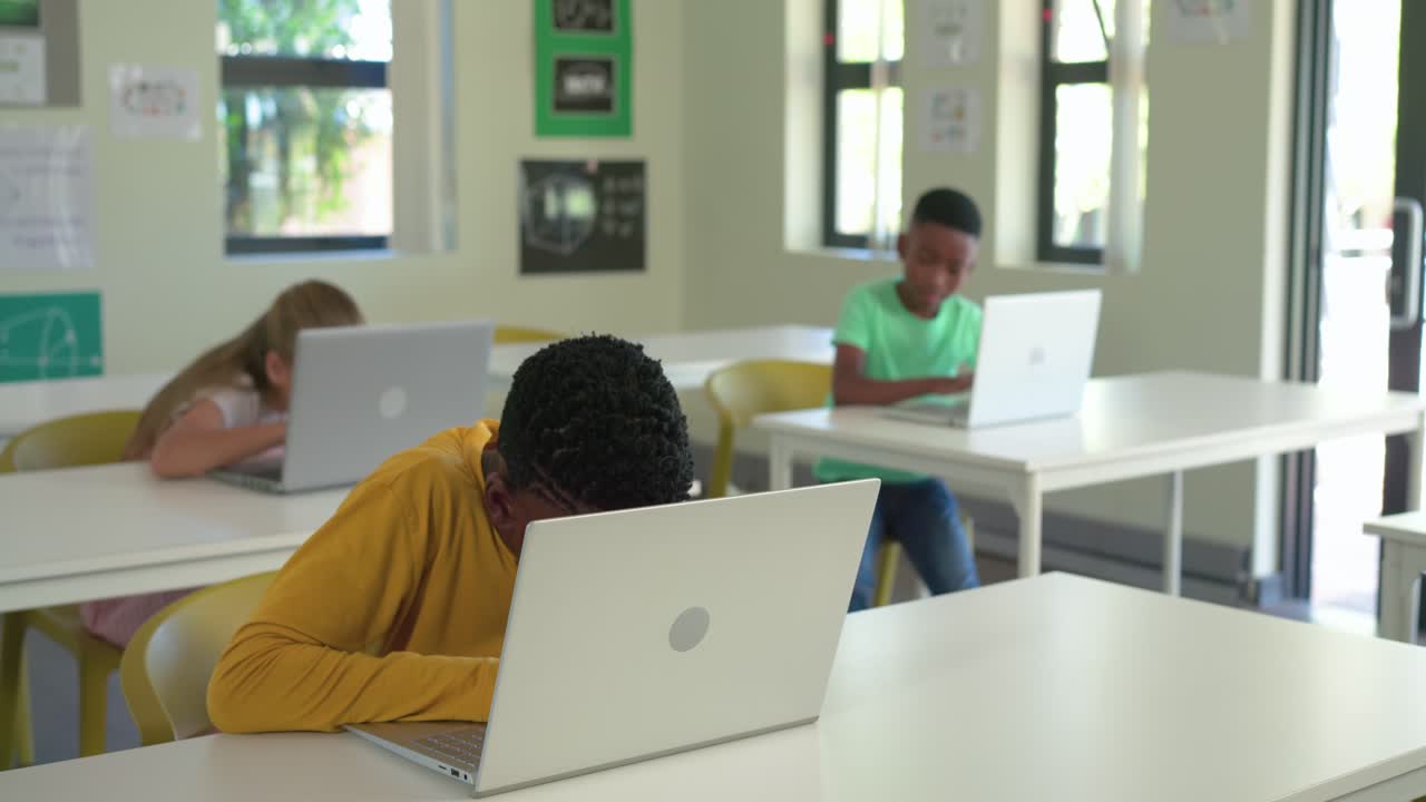 Compagni di classe, ragazzo afroamericano con maglietta gialla che usa un laptop per i compiti in classe