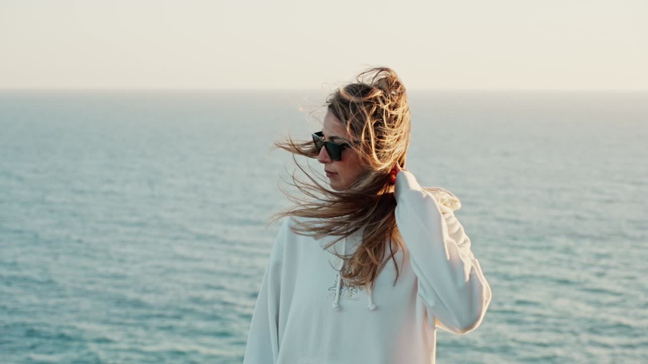 Slow motion shot of a girl's hair being blown over her face at the ocean during sunset
