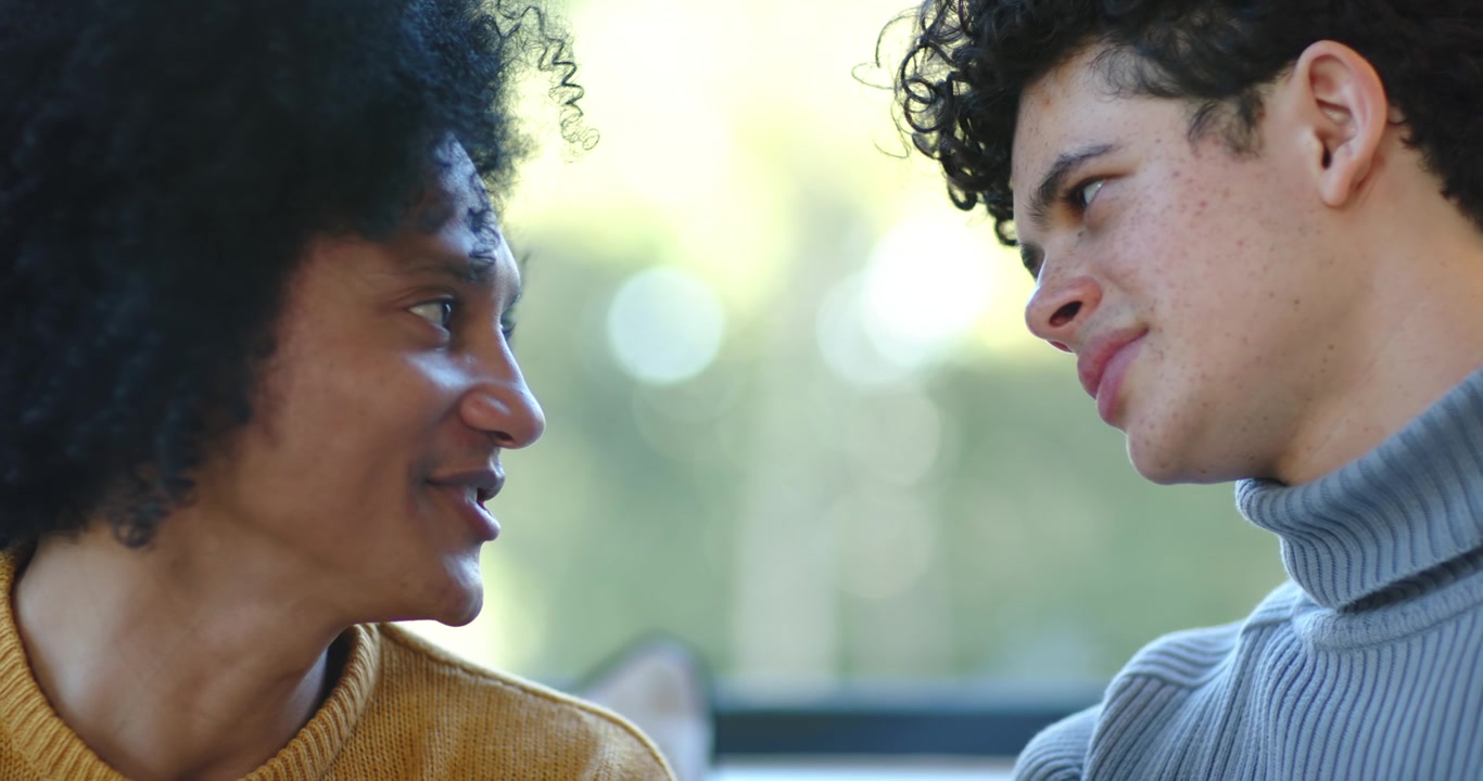 Two men sitting on couch near window sharing conversation, left man initiating connection