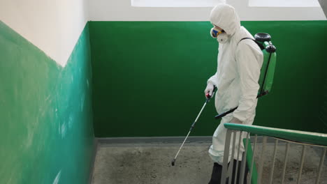 hombre con ropa protectora rocía las escaleras de un edificio de apartamentos con antiséptico