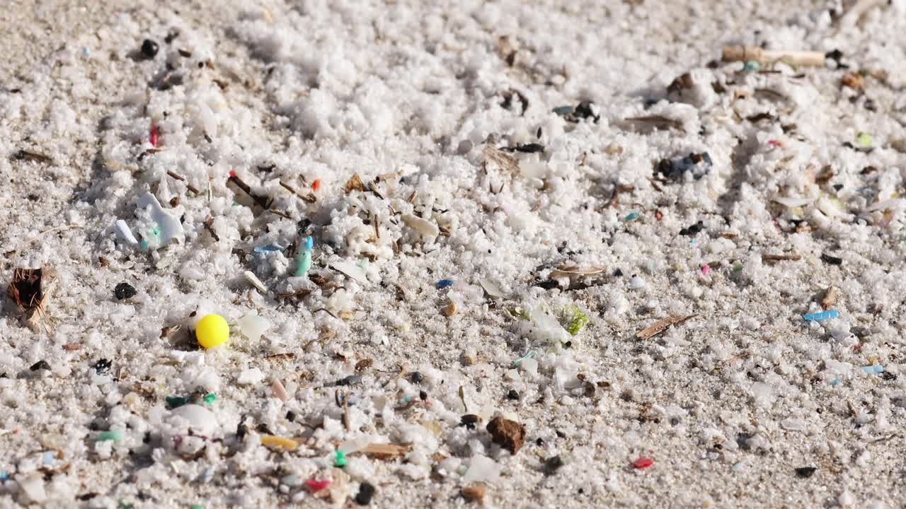 Close-up of microplastics and debris scattered on sandy beach in daylight